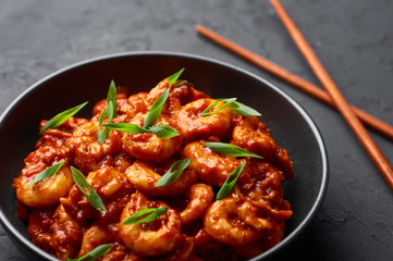 Schezwan Prawns in black bowl at dark slate background. Schezwan Prawns is indo-chinese cuisine curry dish with prawns or shrimps roasted in Schezwan Sauce.