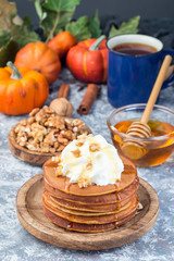 Obraz na płótnie Canvas Delicious homemade pumpkin pancakes served with whipping cream, walnuts and honey, autumn decoration, vertical