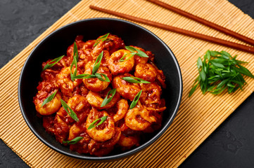 Schezwan Prawns in black bowl at dark slate background. Schezwan Prawns is indo-chinese cuisine curry dish with prawns or shrimps roasted in Schezwan Sauce.