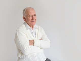 Beautiful gray-haired pensioner with his hands clasped near his chest sitting on a white background