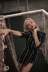 Fashion young beauty woman with blonde hair in classic sundress and heels posing on gate on sports...