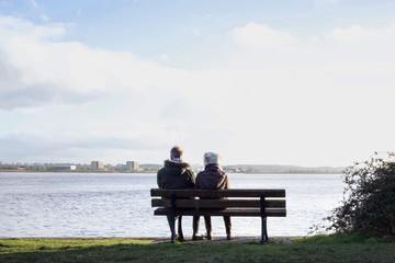 Couple sat on a bench looking at the water views in front.