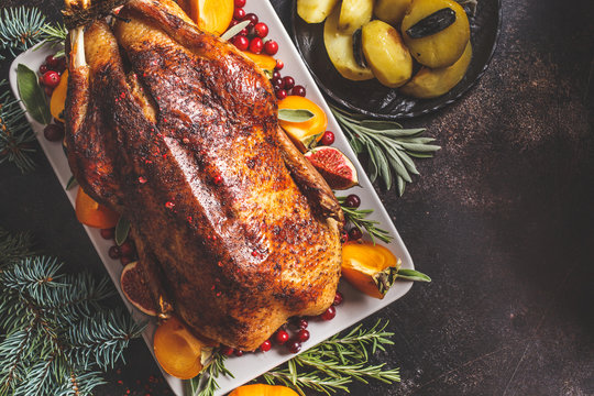 Christmas baked duck with herbs and fruits on gray plate, dark background.