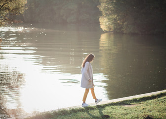 a young woman in an autumn coat and sneakers walks by the river