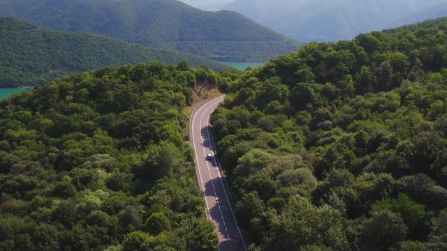 One small gray silver car rides a forest freeway in the Ural Mountains at summer sunny day - Aerial drone view