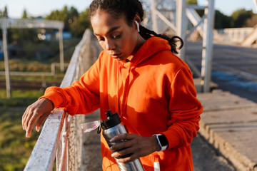 Photo of african american woman using earpods and holding water bottle