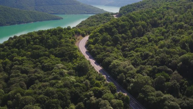 One small gray silver car rides a forest freeway in the Ural Mountains at summer sunny day - Aerial drone view