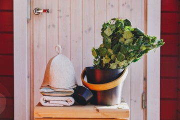Sauna accessories with birch broom, hat and towels near a red wooden sauna in Finland