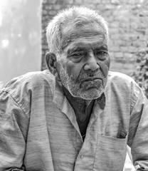 Black and White photograph of Superannuated Senior Citizen in his early 80s. He has wrinkles on his face and neck, is thinking deeply and posing to camera with a gloomy expression of loneliness.