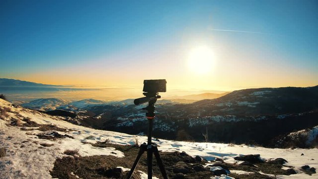 Dslr mirrorless camera on tripod shooting timelapse on mountain winter sunset