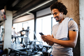 Young handsome man using phone while having exercise break in gym