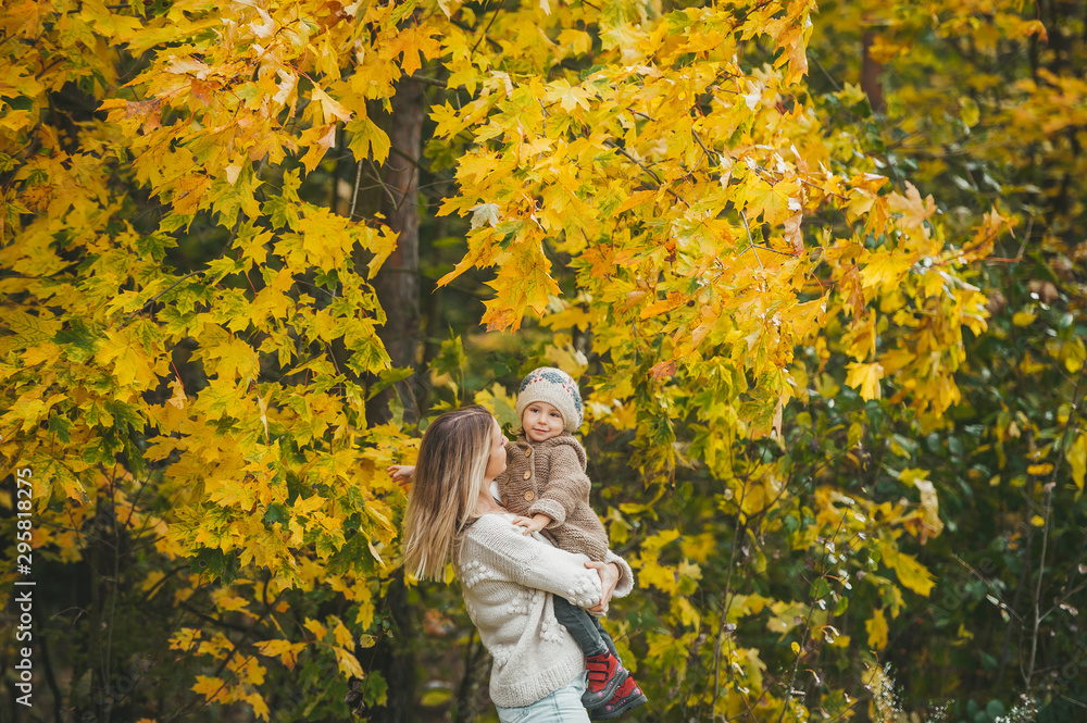 Wall mural young beautiful happy mother holds his little girl in his arms and smiles on autumn sunny day.