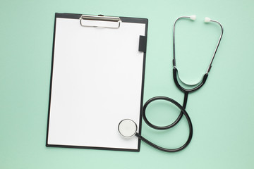High angle view of clipboard with white paper and stethoscope on green surface