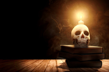 Pile of the book with a human skull and candlelight on a wooden table