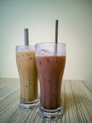 Close up on a tumbler glass full of iced coffee with a reusable metal drinking straw, on a wood restaurant table