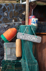 Welcome sign made out of driftwood hanging on a piece of string among discarted buoys, fish traps...