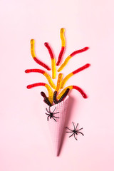 Pink ice cream cone with colorful marmalade worms and spiders. Minimal halloween composition