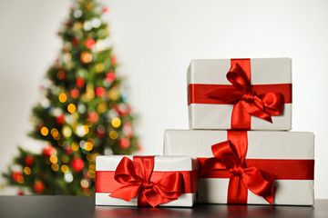Festive composition with stack of many different presents in colorful wrapping paper on foreground and blurry decorated Christmas spruce tree on background. Close up, copy space.