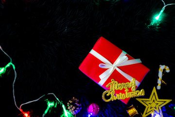 Cozy new year atmosphere. Decoration garland with festive lights, gift box and Merry Christmas concept on black fur background.