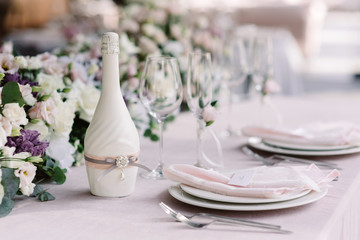 A white bottle of wedding champagne and a luxurious service of the newlyweds table.