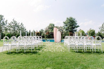 Wedding round arch and transparent chairs made of plastic for guests on the green lawn near the...