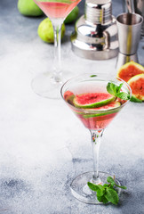 Pink fig martini alcoholic cocktail in shot glass on gray table with bar tools, copy space