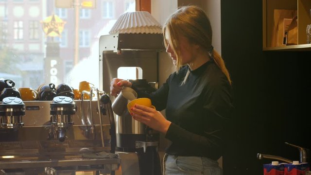 Cute young barista girl in cafe makes coffee cappuccino latte art drawing with milk in the morning