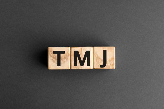 TMJ - acronym from wooden blocks with letters, abbreviation TMJ temporomandibular joint syndrome, TMD Temporomandibular disorder concept, gray background