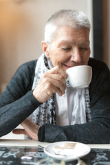 Old lady enjoying her coffee aroma, sitting at the coffee shop