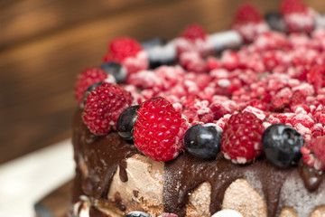 A close-up view of vegan chocolate cake covered with raspberries and blueberries, frozen in the refrigerator, on a table with blurred background. Copy space. Delicious healthy diet. Selective focus