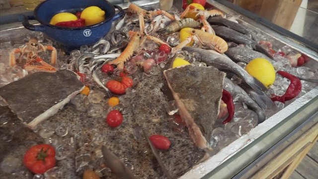 Gobies, mussels, flounder, king prawns, peppers, lemons, tomatoes on an ice counter.