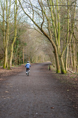 Young girl riding bike away along country path. Vertical shot with copy space