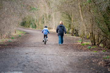 Young girl riding bike next to mum along country path