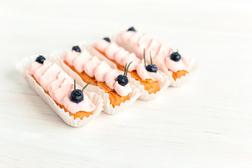 Tasty French eclairs with cream and fresh berries on white wooden table. Set of delicious eclairs. Selective focus.