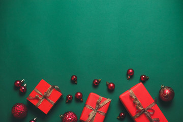 Minimal christmas concept background with red gift box with gold ribbon and red balls on green background. Flat lay style composition, top view.