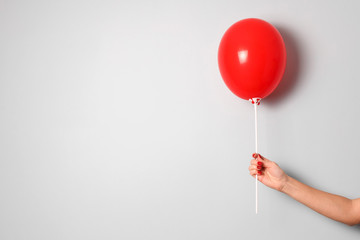 woman hold one red  air ballon in hand with copy space for your text indoor .stylish birthday or holiday background with balloon.red balloon on the gray background in the hand close up.gift concept.