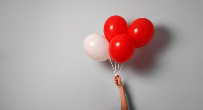 woman hold red and white  air ballons in hand with copy space for your text indoor .stylish birthday party or holidays with balloons.four red  balloons on the gray background with copy space for text.