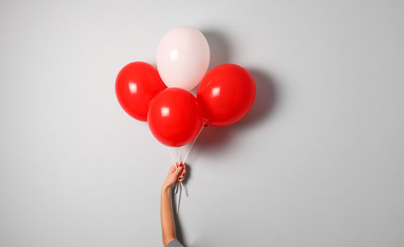 woman hold red and white air ballons in hand with copy space for your text indoor .stylish birthday party or holidays with balloons.four red balloons on the gray background with copy space for text.