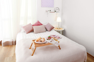 Tray with tasty breakfast on bed