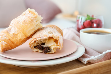 Tasty croissant with cup of coffee on bed table, closeup