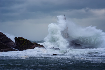 Big wave against old Lighthouse in the port of Ahtopol, Black Sea, Bulgaria on a moody stormy day. Danger, dramatic scene.