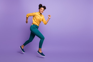 Fototapeta na wymiar Full length profile photo of pretty dark skin lady jumping high speed rushing to finish line wear casual yellow shirt trousers isolated purple color background