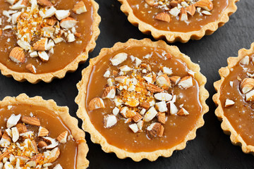 Shortcake sucre dough pastry caramel tartlets tart with caramel brittle, nuts, almonds, caramel crumbs on a black slate plate. Top view portioned dessert for celebration