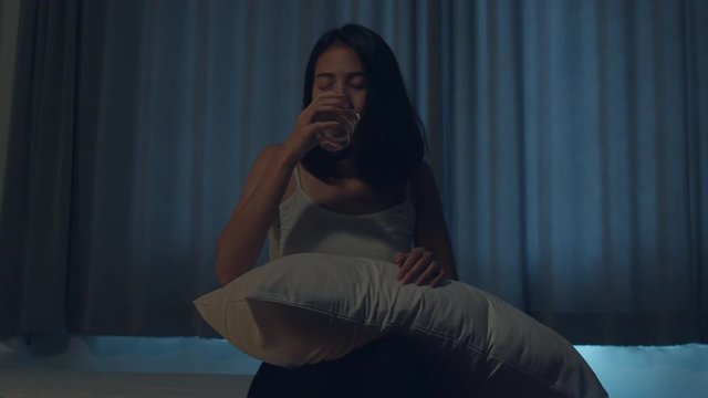 Beautiful Asian young woman sitting on bed take sleeping pill or night medicine in bedroom. Unhealthy sick Indian female suffers from insomnia or headache, depressed girl holds antidepressant meds.