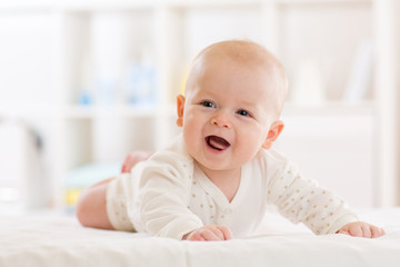 Baby boy wearing white clothes in sunny nursery room. Newborn child relaxing in bed.