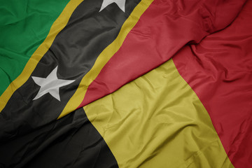 waving colorful flag of belgium and national flag of saint kitts and nevis.
