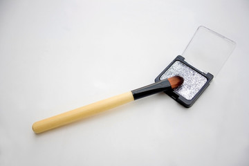 Silver sparkly eyeshadow and make up brush on white background. Selective focus.