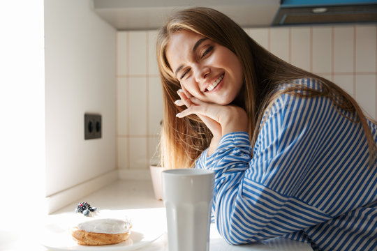 Image of attractive young girl smiling and drinking tea in kitchen