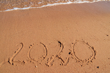 Concept of Christmas and New Year's holidays at tropical resort. 2020 number written on wet sand of sea beach