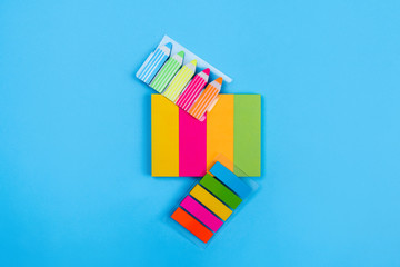 Sets of bright colored stickers in the form of stripes of yellow, pink, orange, green located on a blue background next to which are stickers in the form of stripes and pencils. Close-up.